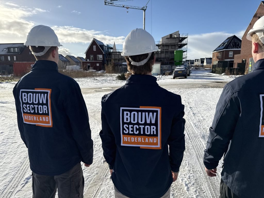 Drie vakmensen van Bouwsector Nederland met witte helm en werkjas bij huizen in aanbouw